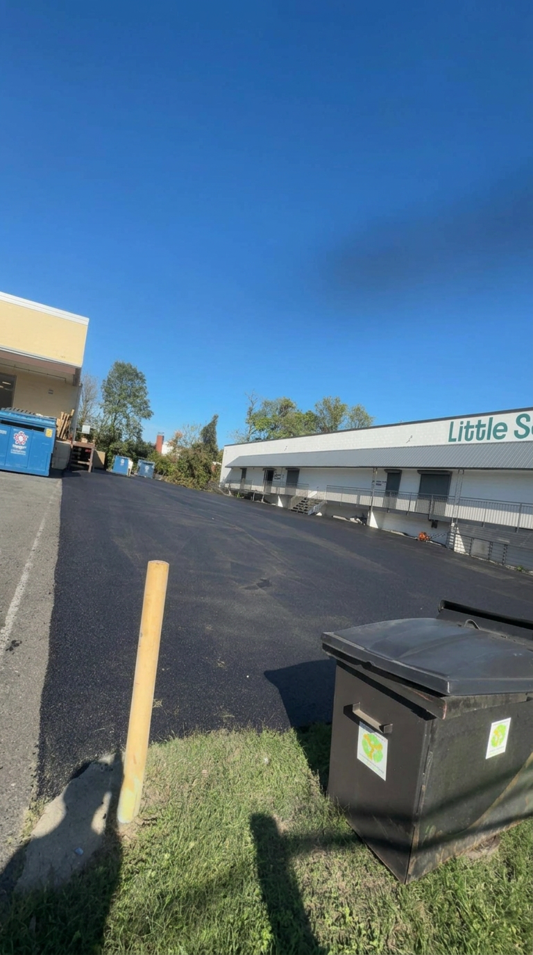 Wide expanse of new black asphalt in a commercial parking lot behind a retail building